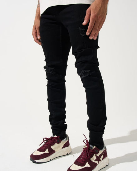 Person wearing black ripped jeans and maroon and white sneakers on a white background