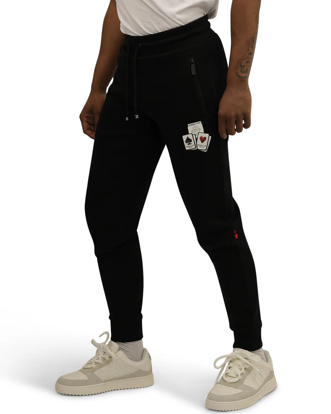 Person wearing black jogger pants with card design patches on a white background