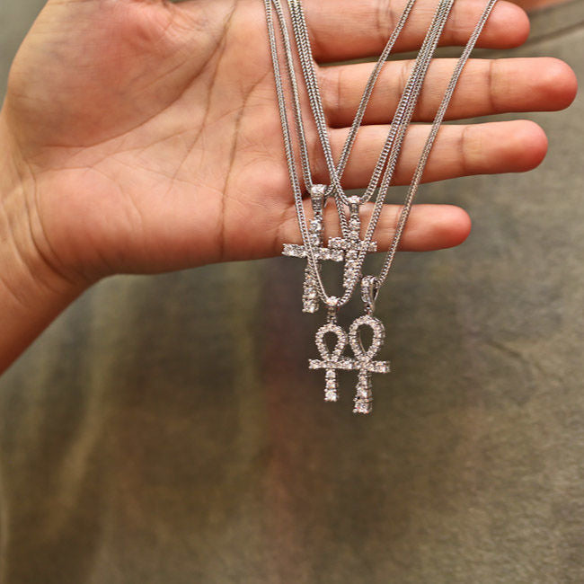Hand holding three silver necklaces with pendants against a neutral background