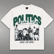 A white short-sleeve graphic t-shirt laid flat on a gray background. The shirt features a large green 'POLITICS' text graphic across the chest, a black-and-white photograph of a crowd underneath, and the phrase 'one of one.
