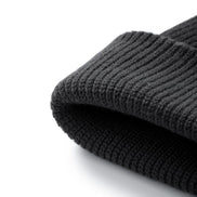 A close-up of a folded dark grey ribbed knit beanie hat on a clean white background.