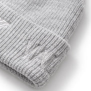 Close-up of a light gray ribbed knit beanie with a folded cuff and a subtle embroidered logo on the cuff, shown on a white background.