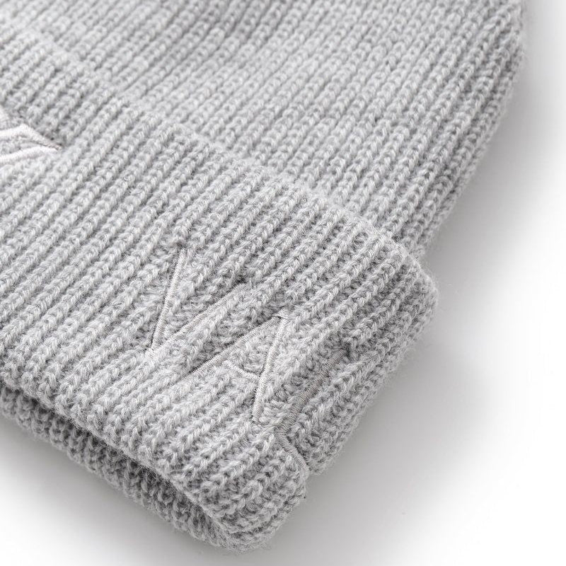 Close-up of a light gray ribbed knit beanie with a folded cuff and a subtle embroidered logo on the cuff, shown on a white background.