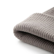A close-up of a folded ribbed-knit beanie in a warm taupe-gray color, showing the detailed knit texture against a clean white background.