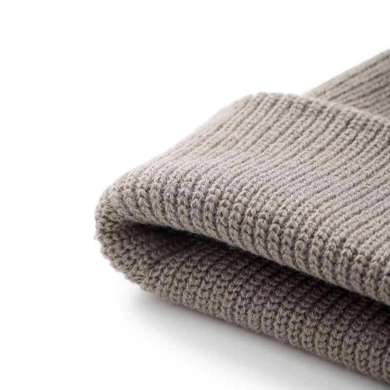 A close-up of a folded ribbed-knit beanie in a warm taupe-gray color, showing the detailed knit texture against a clean white background.