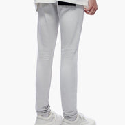 A person shown from the waist down wearing light gray slim-fit jeans, a white graphic t-shirt, and white platform sneakers against a plain white background.