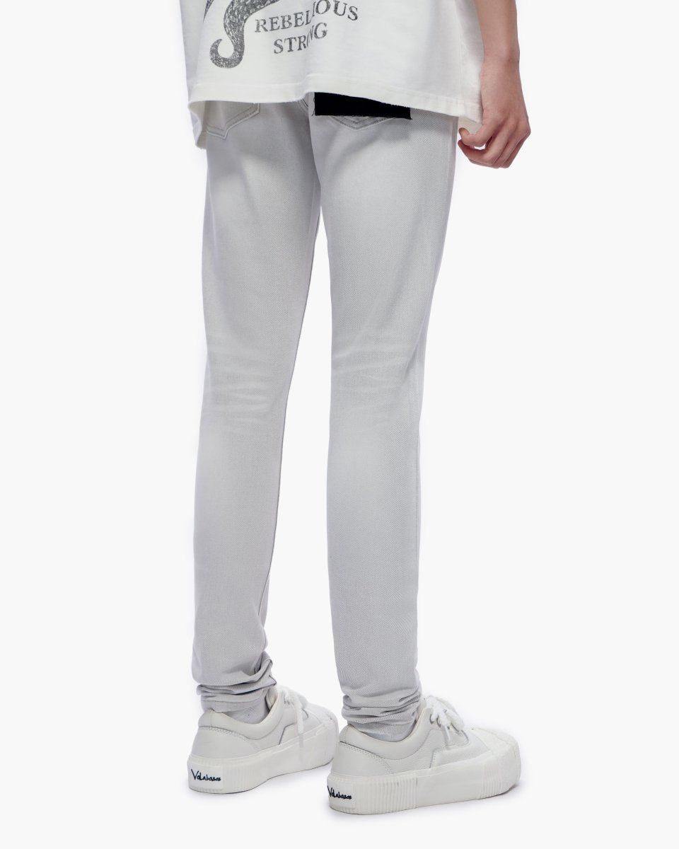 A person shown from the waist down wearing light gray slim-fit jeans, a white graphic t-shirt, and white platform sneakers against a plain white background.