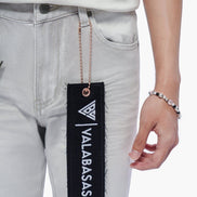 Person wearing light gray jeans with a 'VALABASAS' tag, holding a bracelet.