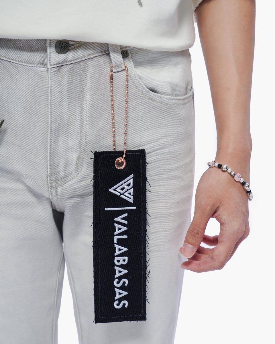 Person wearing light gray jeans with a 'VALABASAS' tag, holding a bracelet.