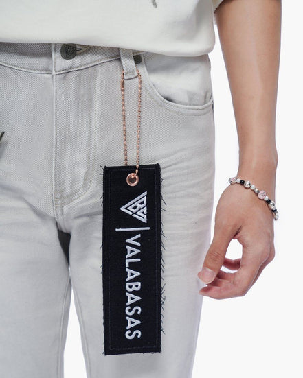 Person wearing light gray jeans with a 'VALABASAS' tag, holding a bracelet.