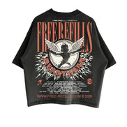 A black short-sleeve graphic T-shirt laid flat against a white background, featuring a large front print with the words 'FREE REFILLS' and 'READY WEAR' in orange-red lettering, a winged cherub motif, and small white text including 'A FREE REFILLS PUBLICATION' and a website at the bottom.