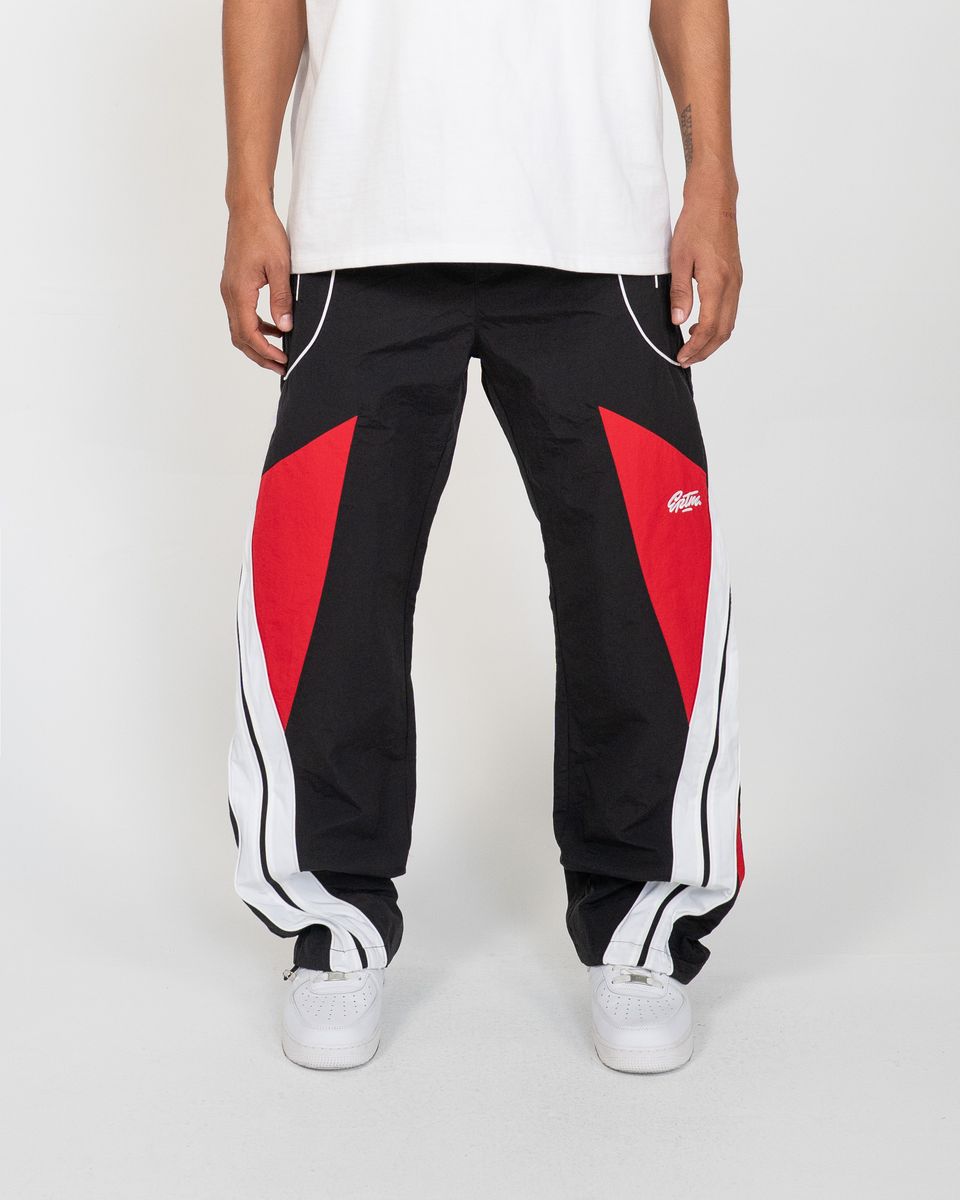 Black track pants with red and white accents worn by a person on a white background