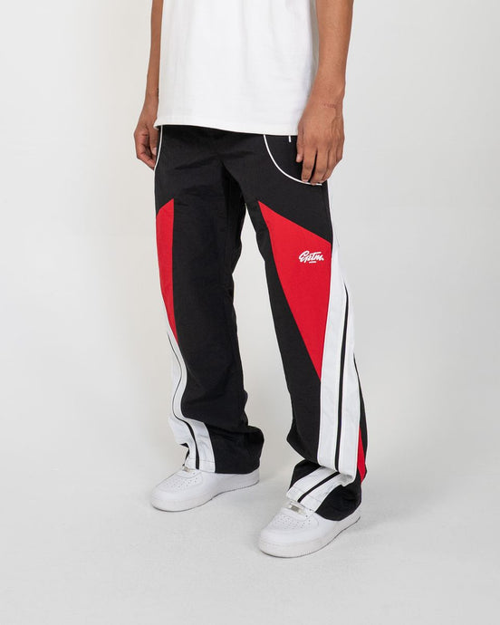 Person wearing black and red track pants with a logo on a white background