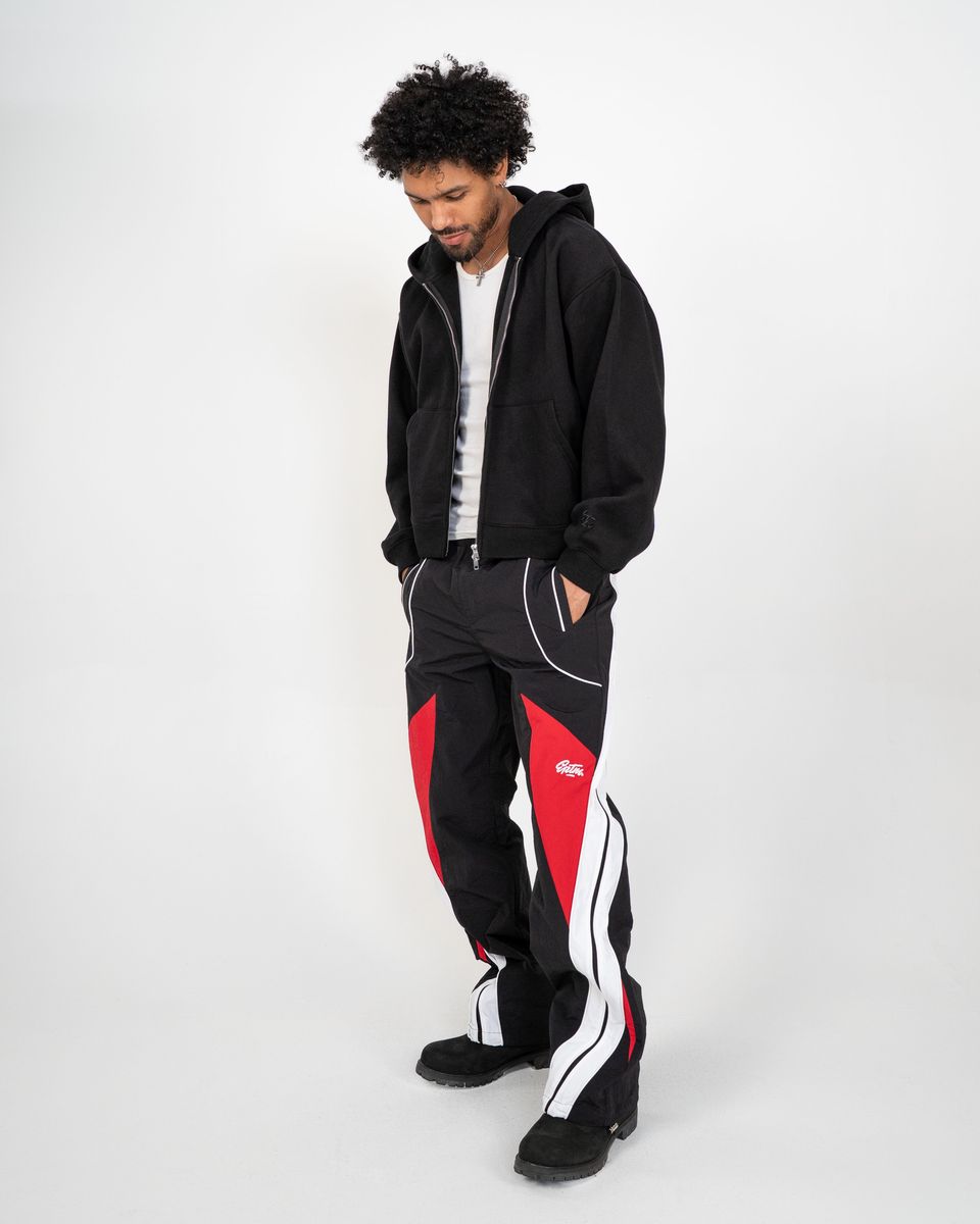 Person wearing a black hoodie and black pants with red and white accents on a white background