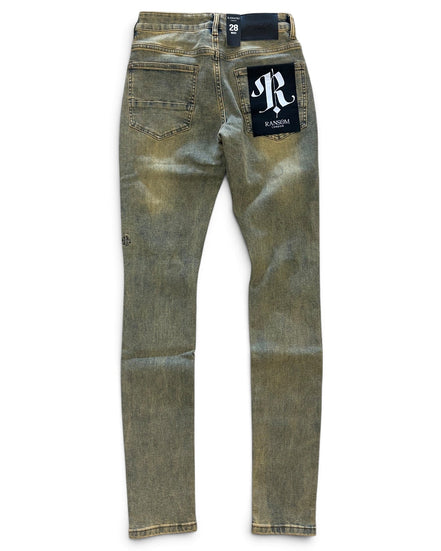 A pair of slim-fit jeans in a washed olive green or khaki-tan denim, shown from the back on a white background. The back right pocket features a black brand patch with a white monogram logo, and a black waistband label reads '28'.