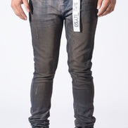 A person wearing slim-fit dark gray washed denim jeans with distressed details, paired with a white t-shirt and white sneakers, shown from the waist down against a white studio background.