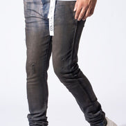 A person wearing slim-fit dark gray washed jeans with distressed details and cuffs, paired with a white t-shirt and white sneakers, shown from the waist down against a white studio background.