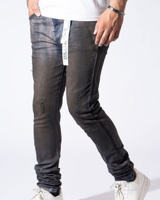 A person wearing slim-fit dark gray washed jeans with distressed details and cuffs, paired with a white t-shirt and white sneakers, shown from the waist down against a white studio background.