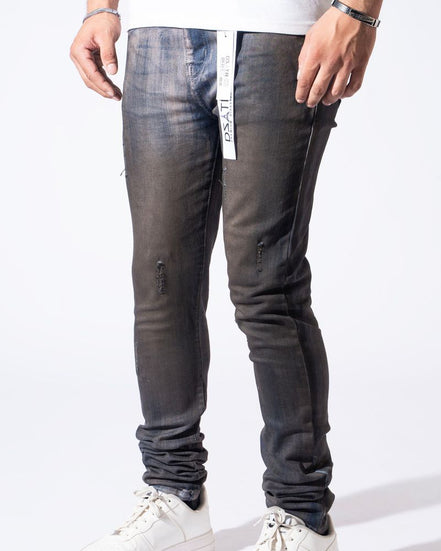 A person wearing slim-fit dark gray washed jeans with distressed details and white sneakers, shown from the waist down against a plain white studio background.