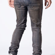 Rear view of a person wearing slim-fit dark gray washed jeans with white sneakers, shown against a plain white studio background.