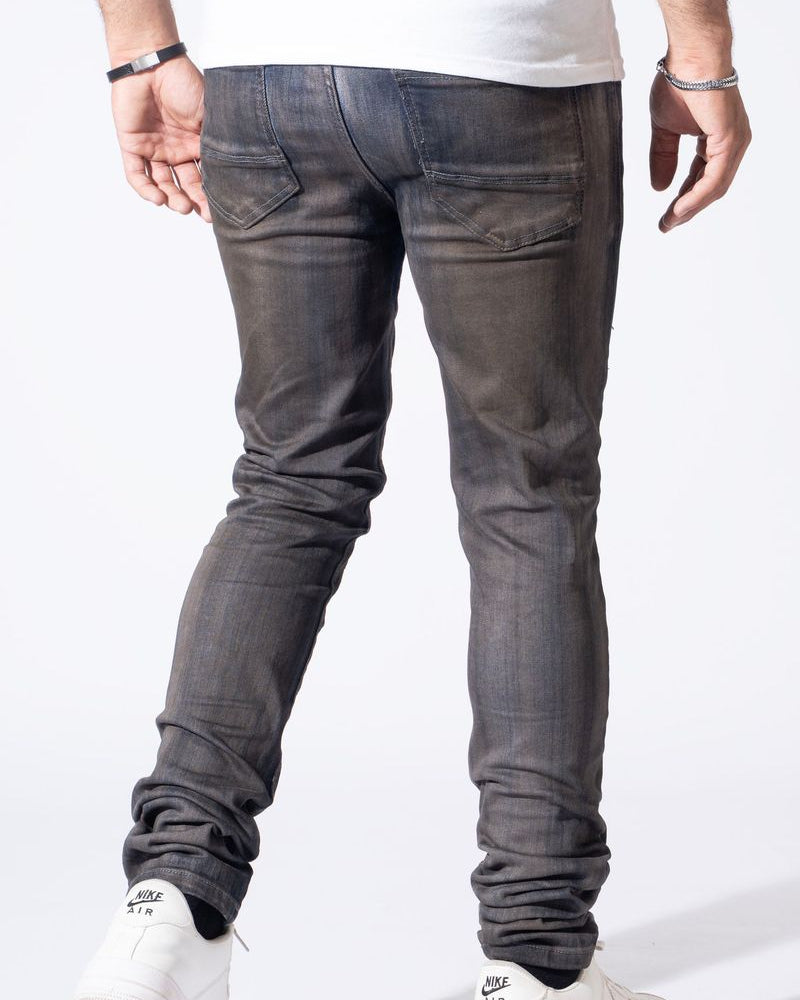 Rear view of a person wearing slim-fit dark gray washed jeans with white sneakers, shown against a plain white studio background.