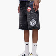 Person wearing black denim shorts with patches, white socks, and white sneakers on a white background