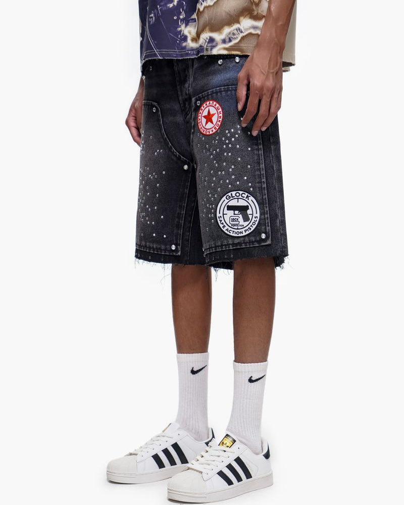 Person wearing black denim shorts with patches, white socks, and white sneakers on a white background