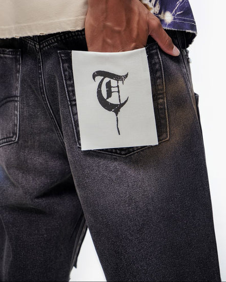 Person wearing black jeans with a white label featuring a logo in the pocket.