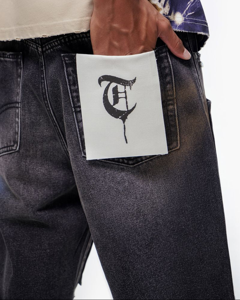 Person wearing black jeans with a white label featuring a logo in the pocket.