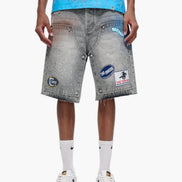 Person wearing gray denim shorts with patches on a white background