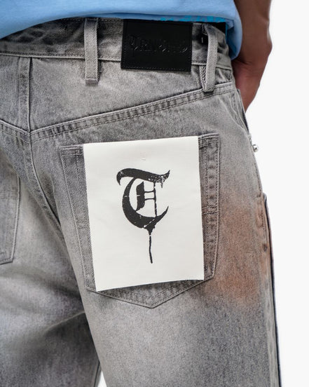 Gray jeans with a white patch featuring a black letter 'T' on a white background
