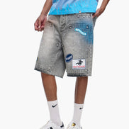 Person wearing gray denim shorts with patches and a blue shirt on a white background