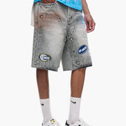Person wearing gray denim shorts with patches, white sneakers, and light blue shirt on a white background