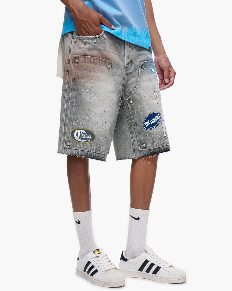 Person wearing gray denim shorts with patches, white sneakers, and light blue shirt on a white background