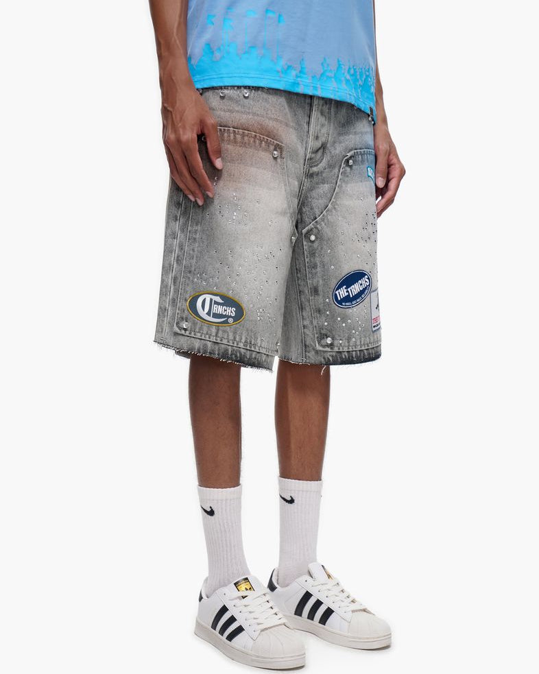 Person wearing gray denim shorts with brand logos, white sneakers, and light blue shirt on a white background
