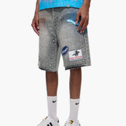 Person wearing gray denim shorts with patches, a blue top, white socks, and white sneakers on a white background.