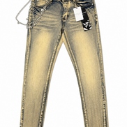 A pair of slim-fit jeans in a faded yellow-tinted wash, featuring a silver chain accessory attached to the right side of the waistband and a black-and-white patterned hangtag.