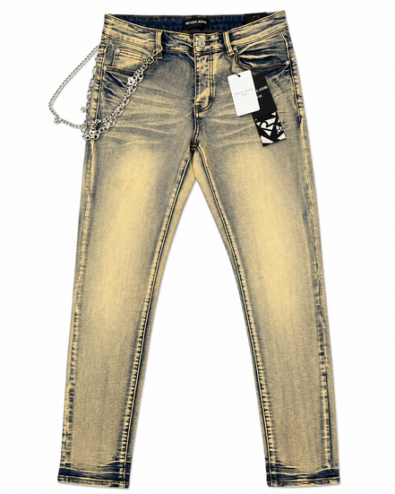 A pair of slim-fit jeans in a faded yellow-tinted wash, featuring a silver chain accessory attached to the right side of the waistband and a black-and-white patterned hangtag.