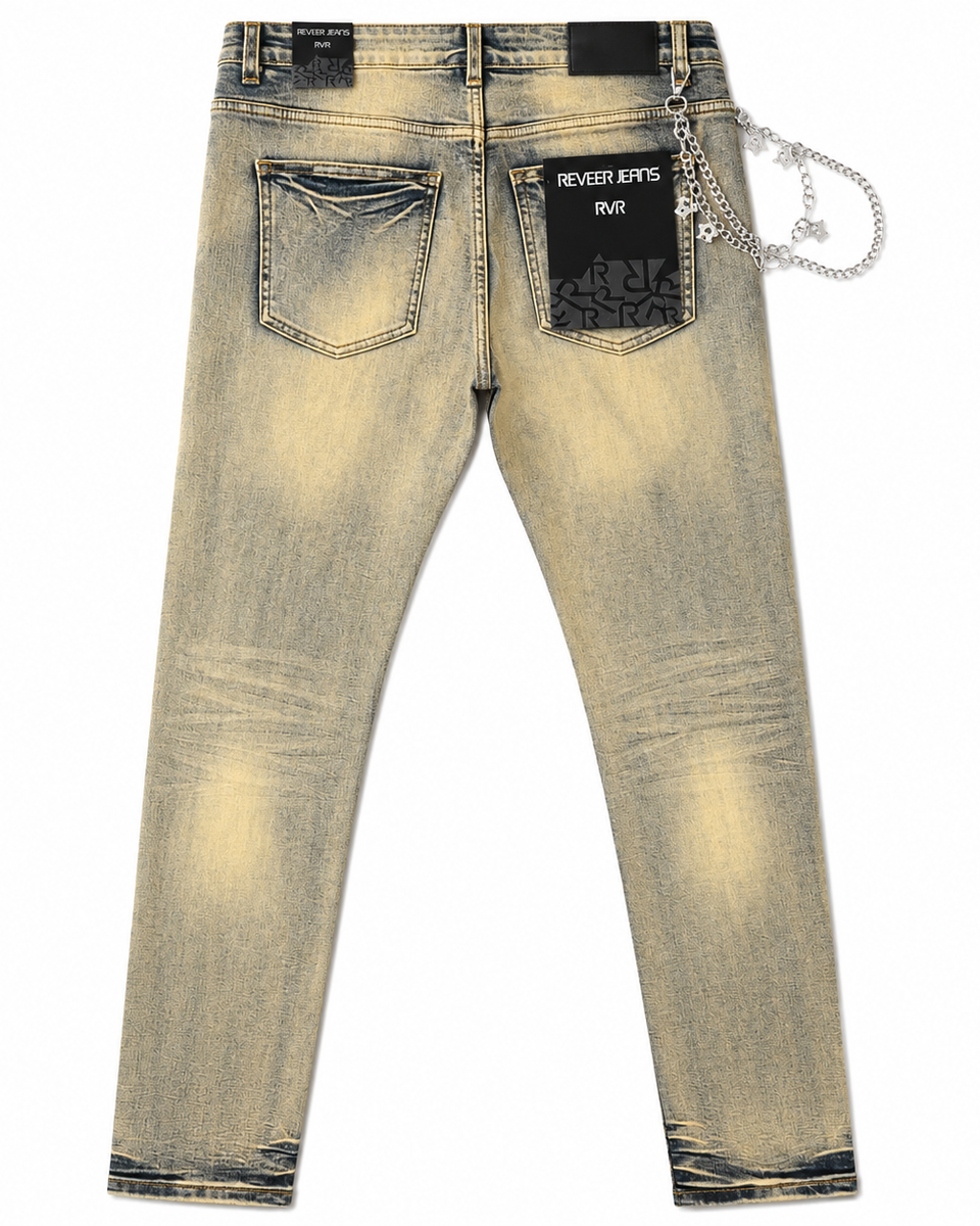 Back view of light-wash denim jeans with a faded yellow-tan wash, black back pocket patches, and a silver chain accessory attached to the back waistband, shown on a white background.