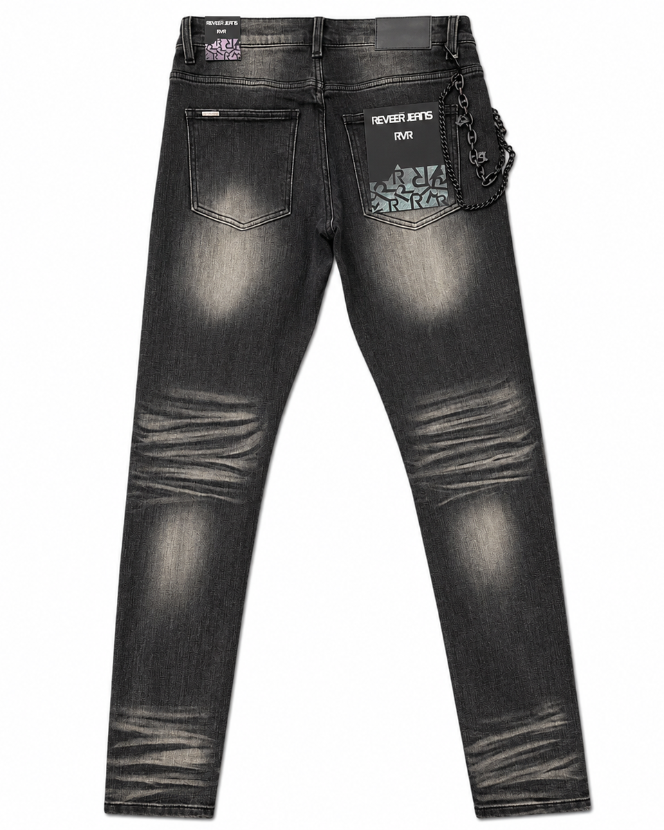 Back view of a pair of dark gray washed denim jeans with distressed fading, featuring a patterned patch pocket on the right side with the text 'NEVER KITS PACK' and a hanging chain detail.