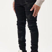 Person wearing black distressed jeans and black and white sneakers on a light gray background