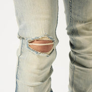 Close-up of light blue jeans with a large rip near the knee on a white background