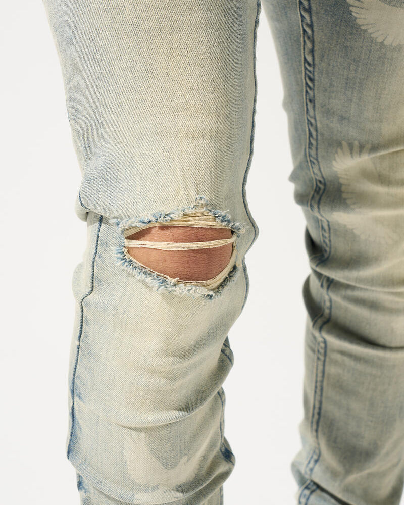 Close-up of light blue jeans with a large rip near the knee on a white background