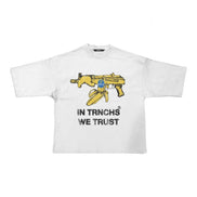 A white short-sleeve t-shirt with a graphic of a yellow assault rifle and a bullet, with the text 'IN TRNCHS WE TRUST' printed below in black.