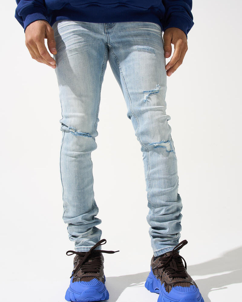 Person wearing light blue ripped jeans and blue sneakers on a white background
