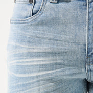 Close-up of light blue jeans with visible stitching and texture on a white background