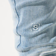 Close-up of a blue denim pocket with a brand logo on a white background