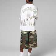 Person wearing a white t-shirt with text and camouflage shorts on a gray background