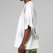 Man wearing a white oversized t-shirt with text and camouflage pants on a gray background