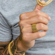 Hand wearing a gold chain bracelet and wearing the gold presidential ring with a gray shirt background